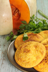 Sopaipillas in a round dish on a wooden table, pumpkin or squash cut in the background and parsley, close-up, vertical. typical chilean food concept