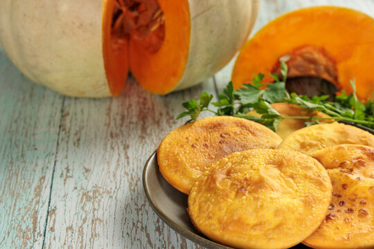 Sopaipillas in a round dish on a wooden table, pumpkin or squash cut in the background and parsley, close-up. typical chilean food concept