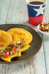 Sopaipillas with pumpkin or squash bite and pebre, on a round plate with a poly paper cup with Chilean flag, on a wooden table and copy space. in vertival. concept of Chilean national holidays