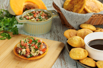 Sopaipillas still life with pumpkin or squash, peregil. in round plate on wooden table, bowls with pebre and chancaca. Concept of typical Chilean food