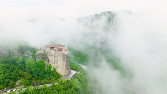 Aerial view of a valey Meteora with clifs covered by mist.  Epic view of Holy Monastery of Rousanos - Saint Barbara complex on the top of meteora cliff among clouds and mist. A UNESCO World Heritage S