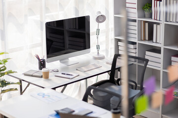 Laptop Computer, notebook, and eyeglasses sitting on a desk in a large open plan office space after working hours	
