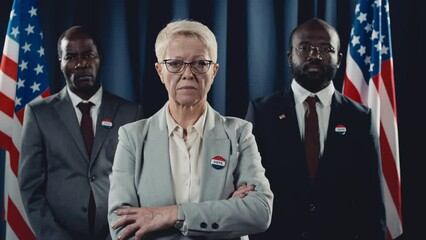 Medium portrait shot of determined middle-aged Caucasian female presidential candidate and African American male vice president and adviser standing in front of USA flag during election