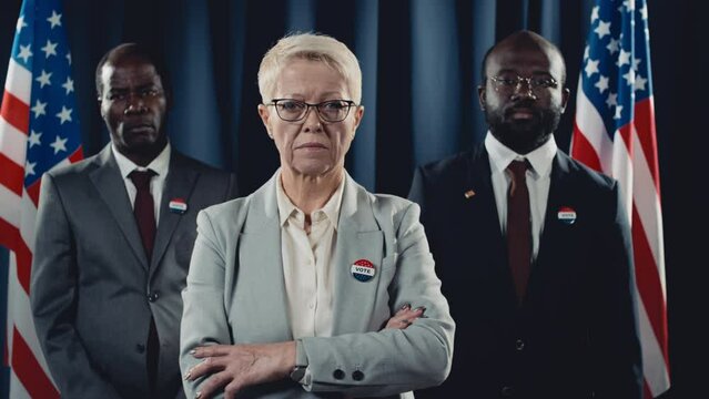 Medium portrait shot of determined middle-aged Caucasian female presidential candidate and African American male vice president and adviser standing in front of USA flag during election - Powered by Adobe
