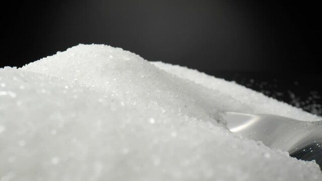 In a macro video, a silver spoon delicately scoops up fine white sugar crystals. Each sparkling grain glistens as it gracefully clings to the spoon's concave surface. Sweet concept. Sugar background

