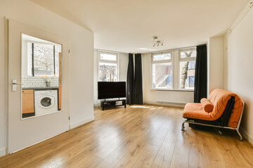 a living room with wood flooring and white walls, including a bright orange chair in the middle part of the room