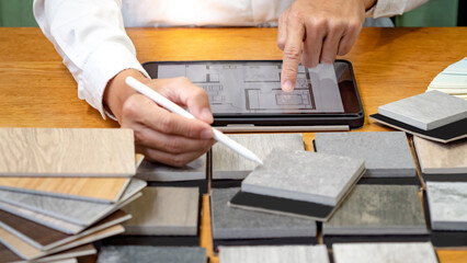 Architect hand choosing and picking stone and wood material samples while drawing on a digital tablet on the table in studio. Designer working for interior architecture and furniture design project