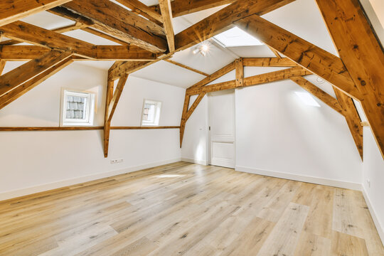 an empty room with wood beams on the ceiling and hardwood flooring in this attic space is very white color