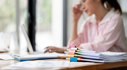 Stressed Businesswoman working in Stacks of paper files for searching and checking unfinished...