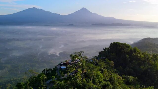 Cinematic drone shot of MENOREH HILL with green landscape and flying clouds in sunlight - Central Java, Indonesia - Aerial panoramic establishing shot