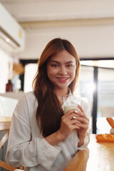Portrait of a young cheerful asian woman drinking milk in kitchen room with healthy raw food. Vegetarianism, wellbeing and healthy lifestyle concept