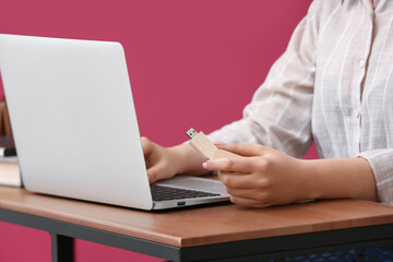 Woman using USB flash drive with modern laptop at wooden table near color wall, closeup