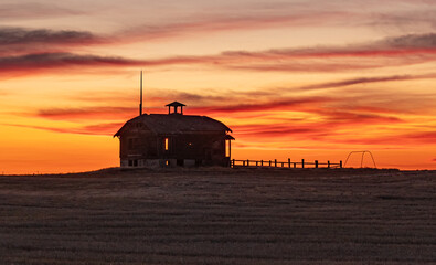Old Abandoned Schoolhouse, with corral and swing silhouetted  in the setting sun. Wasco County, Oregon