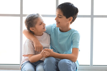 Little boy with his sister hugging near window