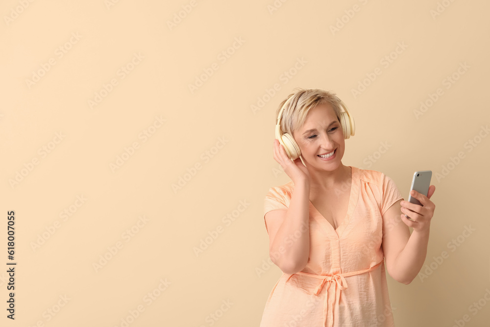 Wall mural mature woman in headphones with mobile phone on beige background