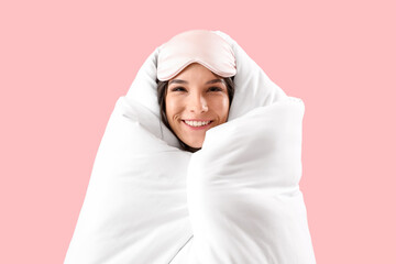 Beautiful happy young woman with soft blanket and sleeping mask on pink background