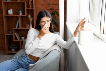 Allergic young woman sneezing with tissue at home