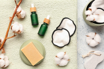 Bottles of essential oil, soap, clean towel, cotton flowers and pads on light background