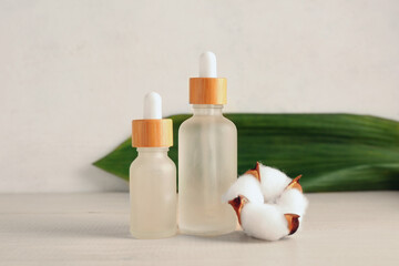 Bottles of essential oil and cotton flower on wooden background