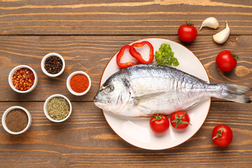 Plate of raw dorado fish with tomatoes and spices on wooden background