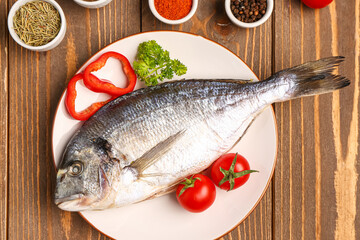 Plate of raw dorado fish with tomatoes on wooden background