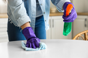 Woman in purple rubber gloves cleaning table with rag and detergent