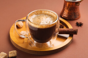 Board with glass cup and jezve of hot espresso on brown background