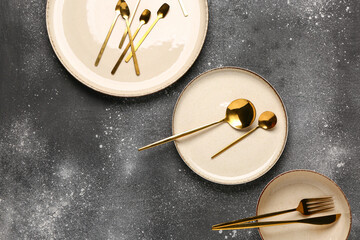 Clean plates, bowl and golden cutlery on dark grey table
