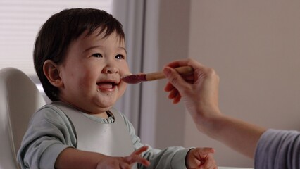 A happy baby smiling in the highchair and eating from the spoon