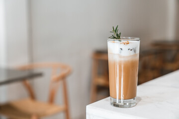 Glass of latte macchiato served layered and topped with cream and rosemary on a bar counter in a...