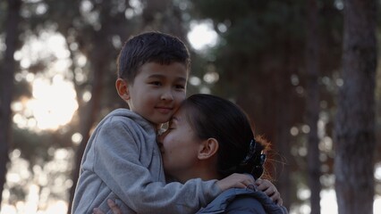 A loving mother holding her son and and kissing him tenderly in nature 