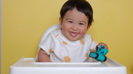 Cute asian baby sits on highchair and smiling on yellow background