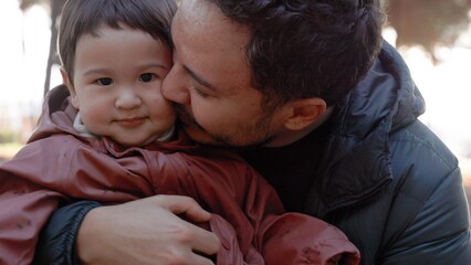 A loving father holding a baby in his arms and and kissing him tenderly in nature