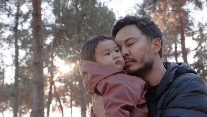 A loving father holding a baby in his arms and and kissing him tenderly in nature