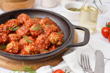 Frying pan of tasty meat balls with tomato sauce and dill on white background