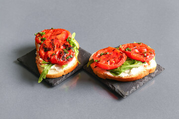 Sandwiches with tasty grilled tomatoes and arugula on grey background
