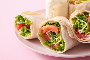 Plate of tasty lavash rolls with tomatoes and greens on pink background