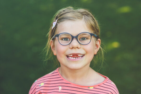 Portrait of a cute preschool girl with eye glasses and big teeth gap outdoors in park. Happy funny child on sunny summer day. Kid loosing milk tooth