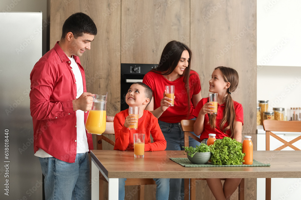 Poster happy parents with their little children drinking orange juice in kitchen