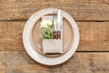 Beautiful table setting with cutlery and floral decor folded in napkin on wooden table - obrazy, fototapety, plakaty