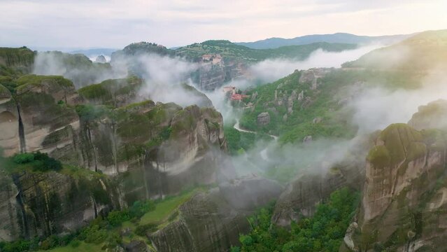 Flight over a valey Meteora with clifs covered by mist.  Epic view of monastery complex on the top of meteora cliffs among clouds and mist. A UNESCO World Heritage Site. Greece. 