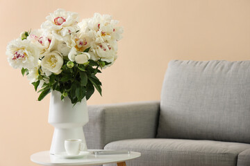 Vase of white peonies with cup of coffee and mobile phone on table near couch