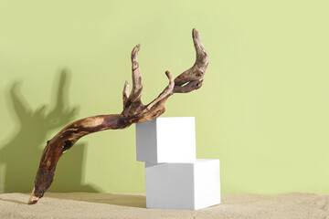 Decorative plaster podiums with branch on sand against olive background