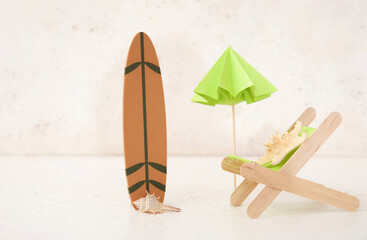 Creative composition with miniature surfboard, deckchair and umbrella on light grunge background