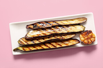 Plate with delicious grilled eggplants on pink background