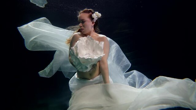 beautiful mermaid with white flower in dark depth of sea, fascinating underwater fairy, portrait
