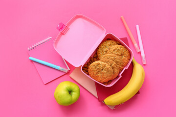 Stationery and lunch box with tasty food on pink background