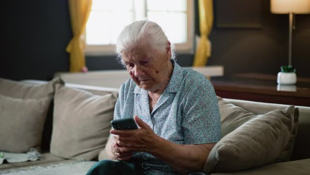 Confused elderly old 80s woman  holding smartphone, don't know how to use