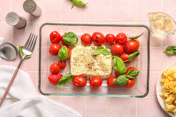 Baking dish with tasty tomatoes and feta cheese on pink tile background
