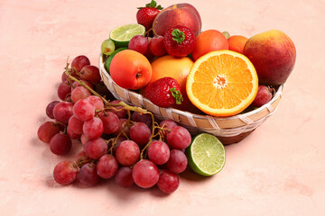 Wicker bowl with different fresh fruits on pink background